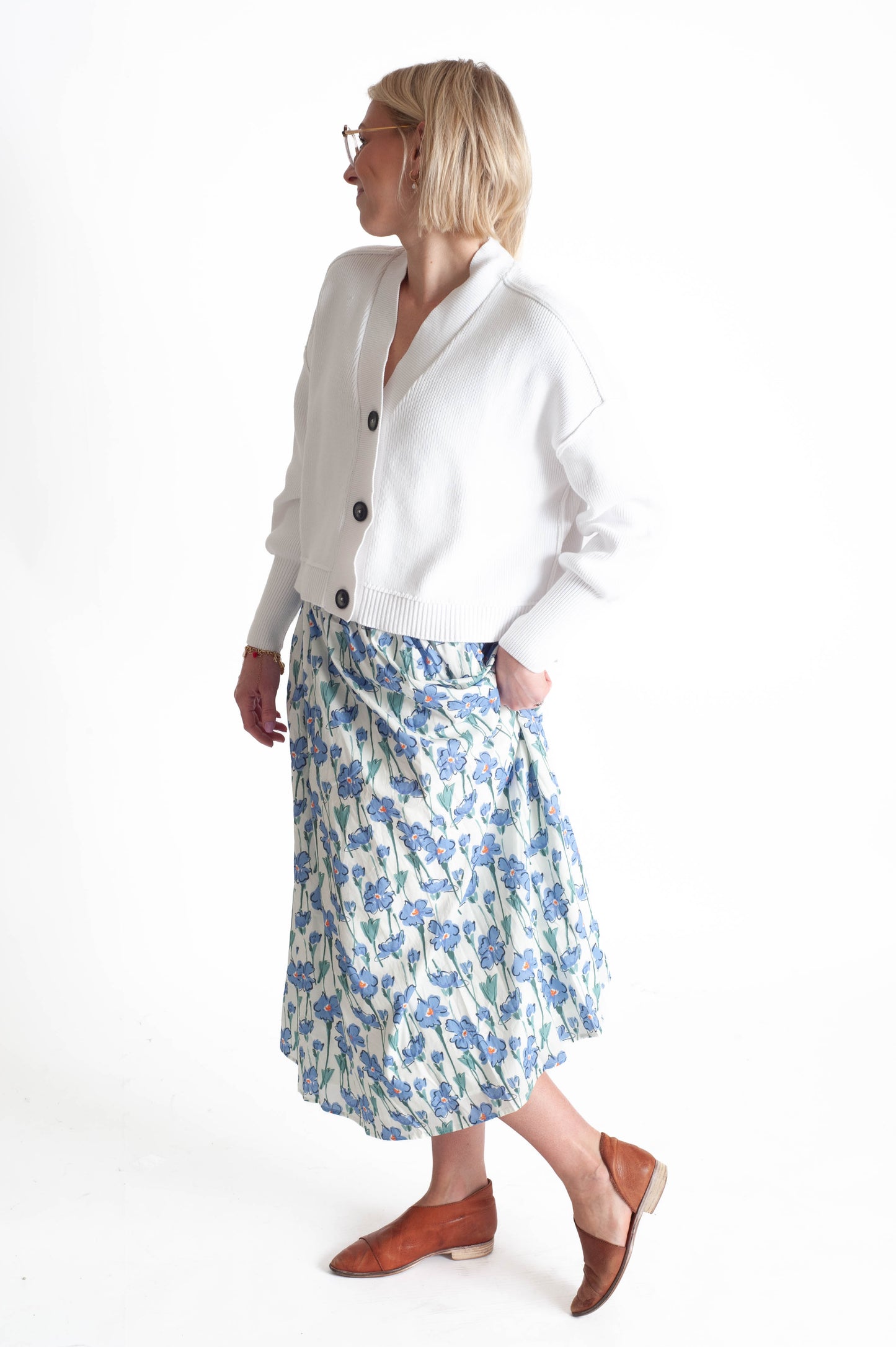 Woman wearing a white cardigan and blue floral skirt on a white background