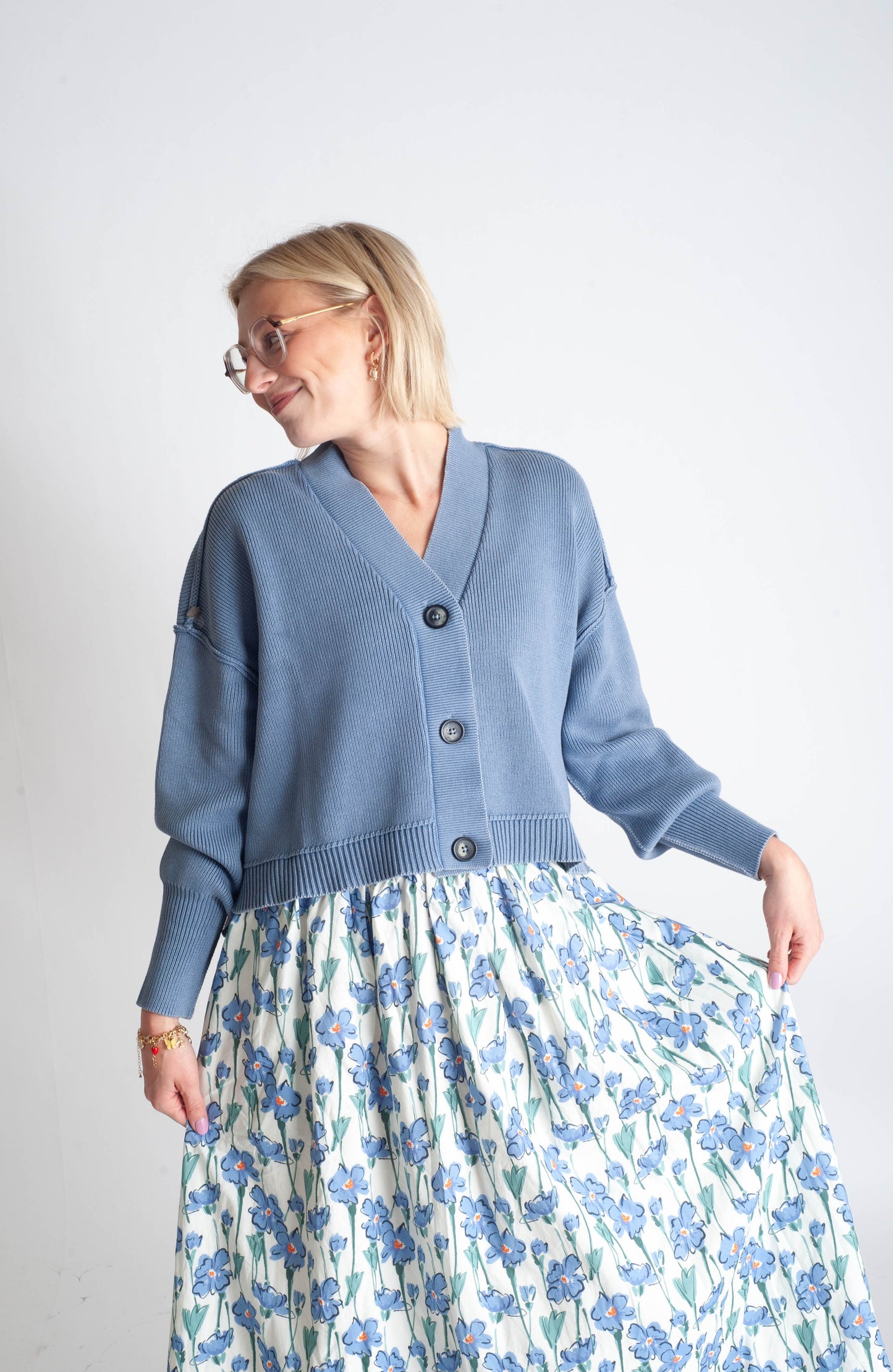 Woman wearing a blue cardigan and floral skirt on a plain background