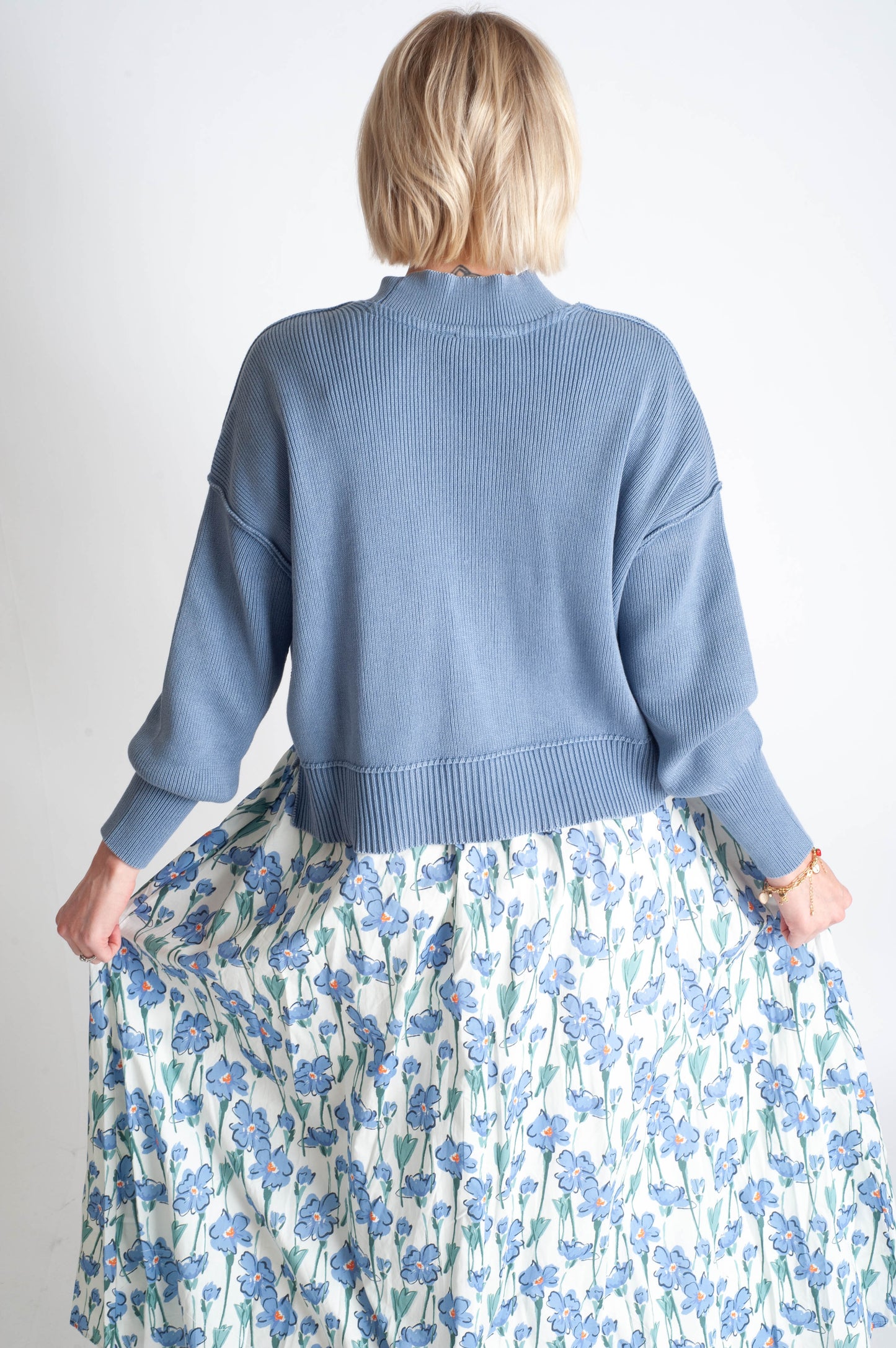 Person wearing a blue sweater and floral skirt on a plain background