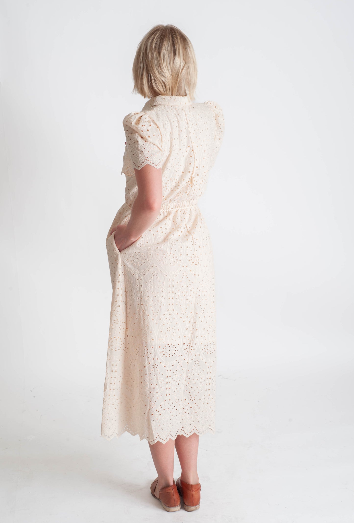 Woman wearing a long, light-colored lace dress against a white background