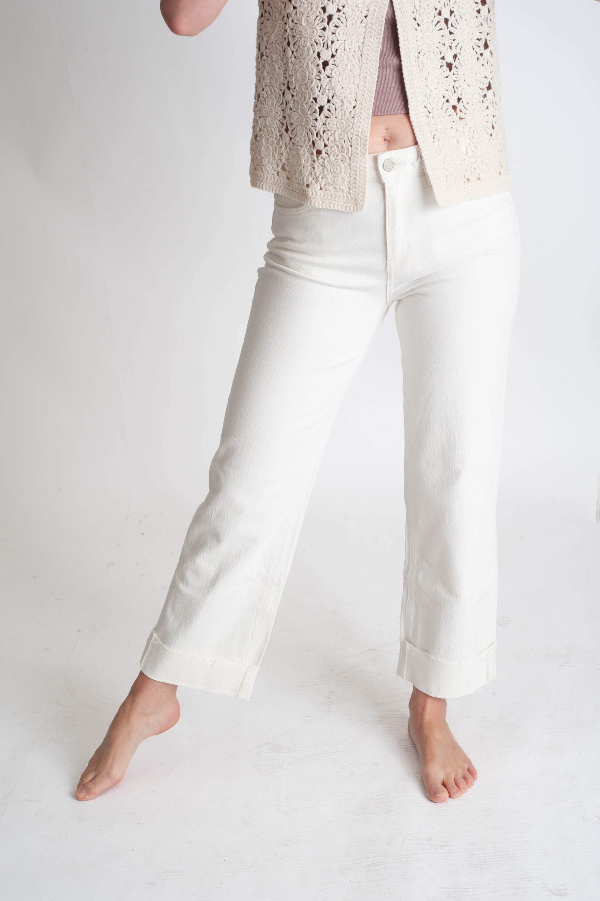 Person wearing white pants and a beige lace top on a plain background