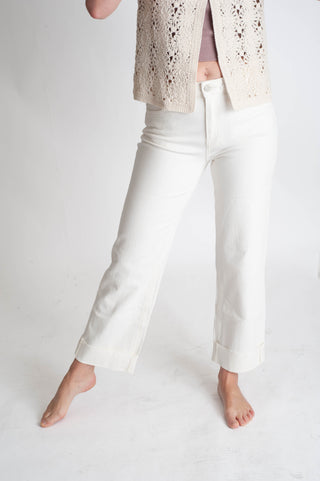 Person wearing white pants and a beige lace top on a plain background