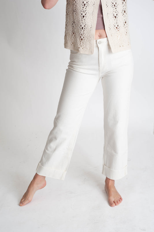 Person wearing white pants and a beige lace top on a plain background