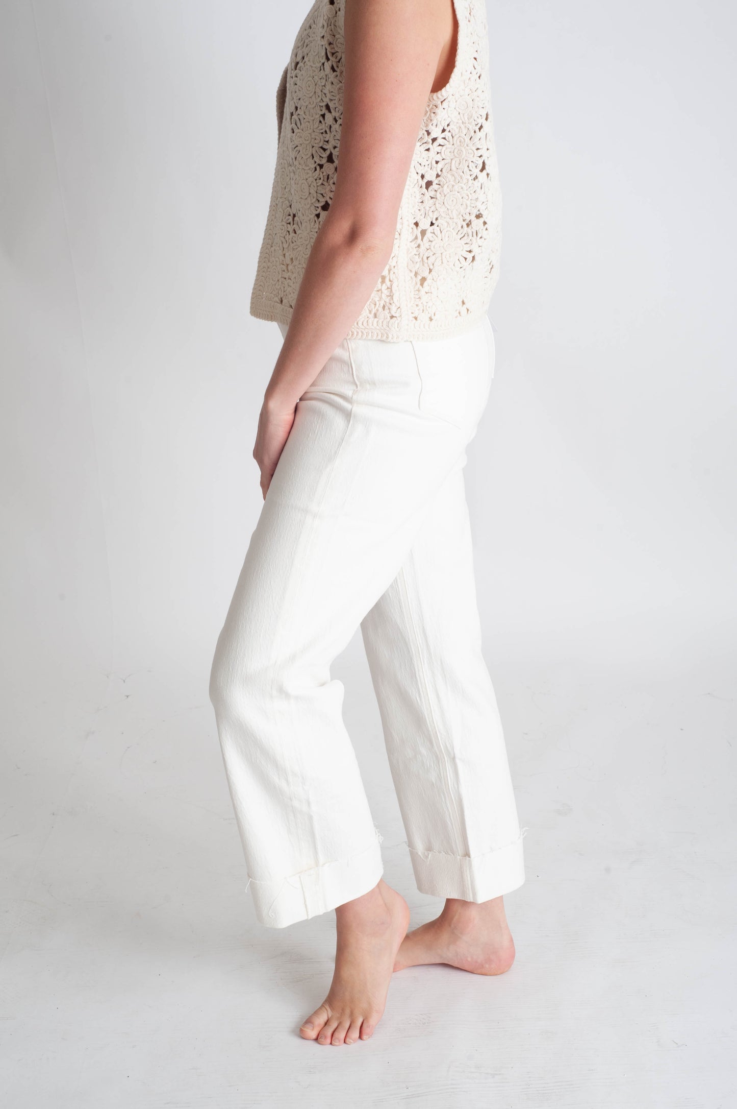 Person wearing a light-colored sleeveless top and white pants on a plain background