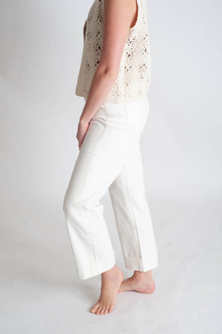 Person wearing a light-colored sleeveless top and white pants on a plain background