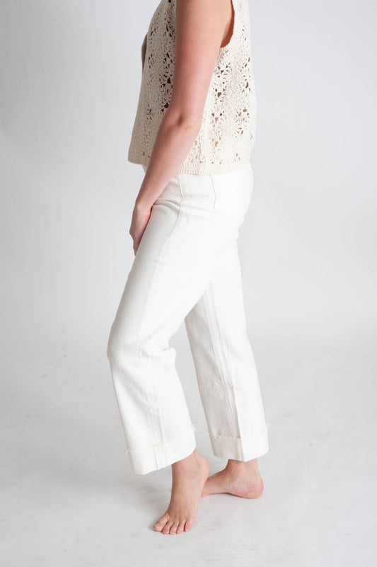 Person wearing a light-colored sleeveless top and white pants on a plain background