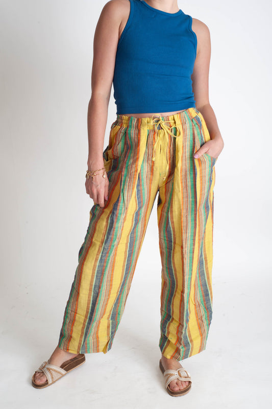 Person wearing a blue sleeveless top and colorful striped pants on a white background