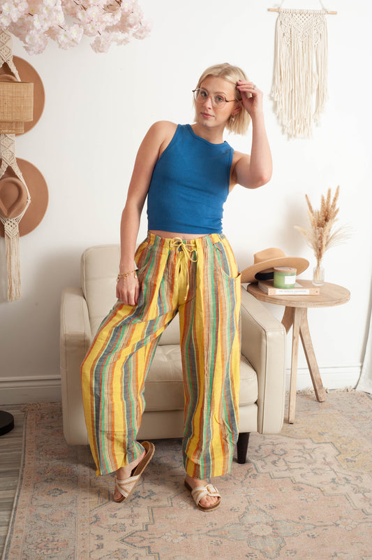 Woman in blue top and colorful striped pants standing in a room with decor elements.