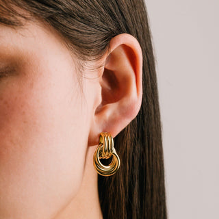 Gold hoop earrings worn by a person with a neutral background
