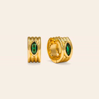 Gold hoop earrings with green gemstones on a beige background