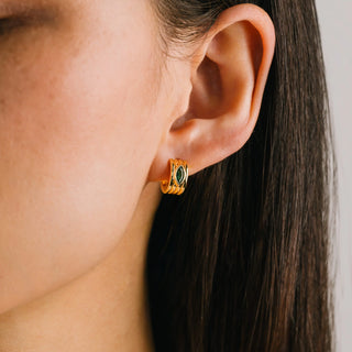 Close-up of an ear wearing a gold earring with green gemstone on a neutral background