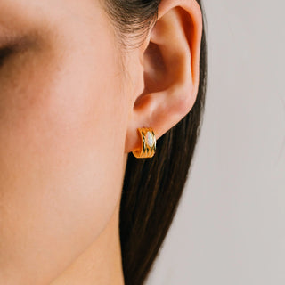 Close-up of an ear wearing a gold hoop earring with a neutral background