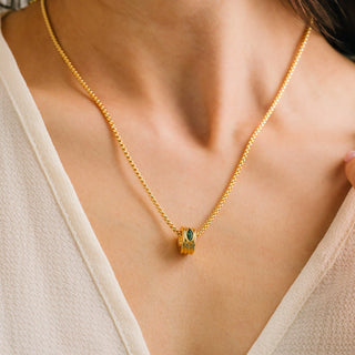 Gold necklace with a pendant on a person wearing a beige top