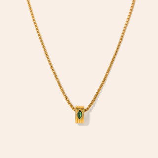 Gold necklace with a green gemstone pendant on a beige background