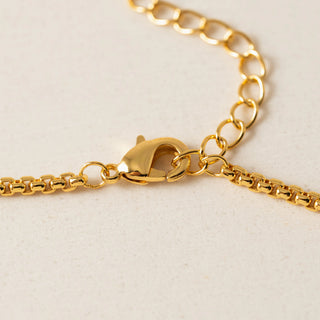 Close-up of a gold chain necklace with a lobster clasp on a light beige textured background.