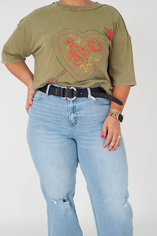 Person wearing a green t-shirt with a heart design and light blue jeans on a white background