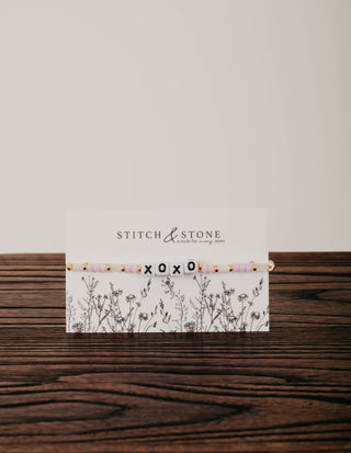 Stitch & Stone card with floral design on a wooden surface with a beaded bracelet that says xoxo