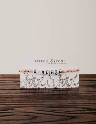 Cuff bracelet with 'GIRL MOM' on a wooden surface, branded 'Stitch & Stone'.