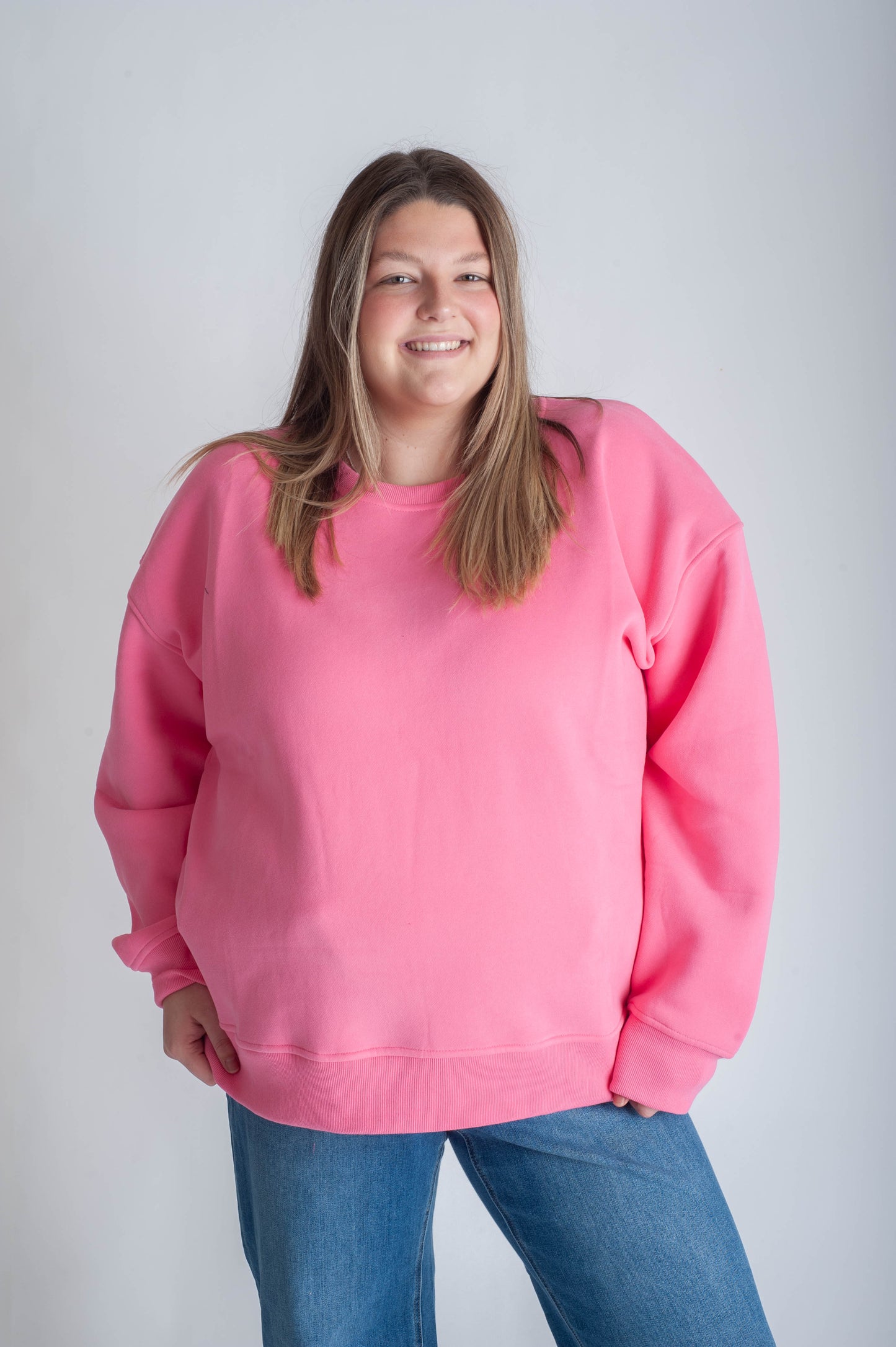 Person wearing a pink sweatshirt and blue jeans against a plain background