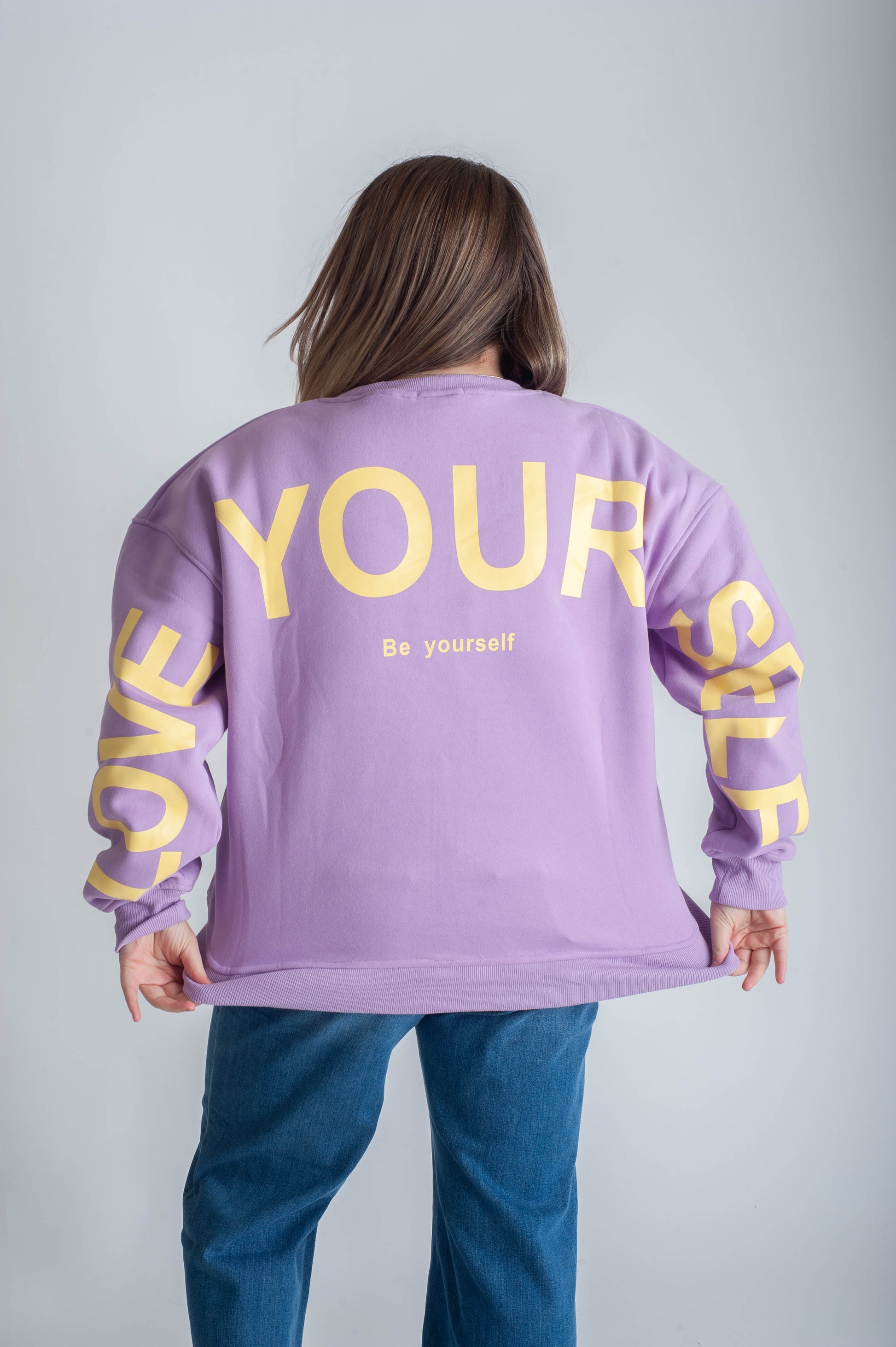 Person wearing a purple sweatshirt with 'BE YOURSELF' text on a white background