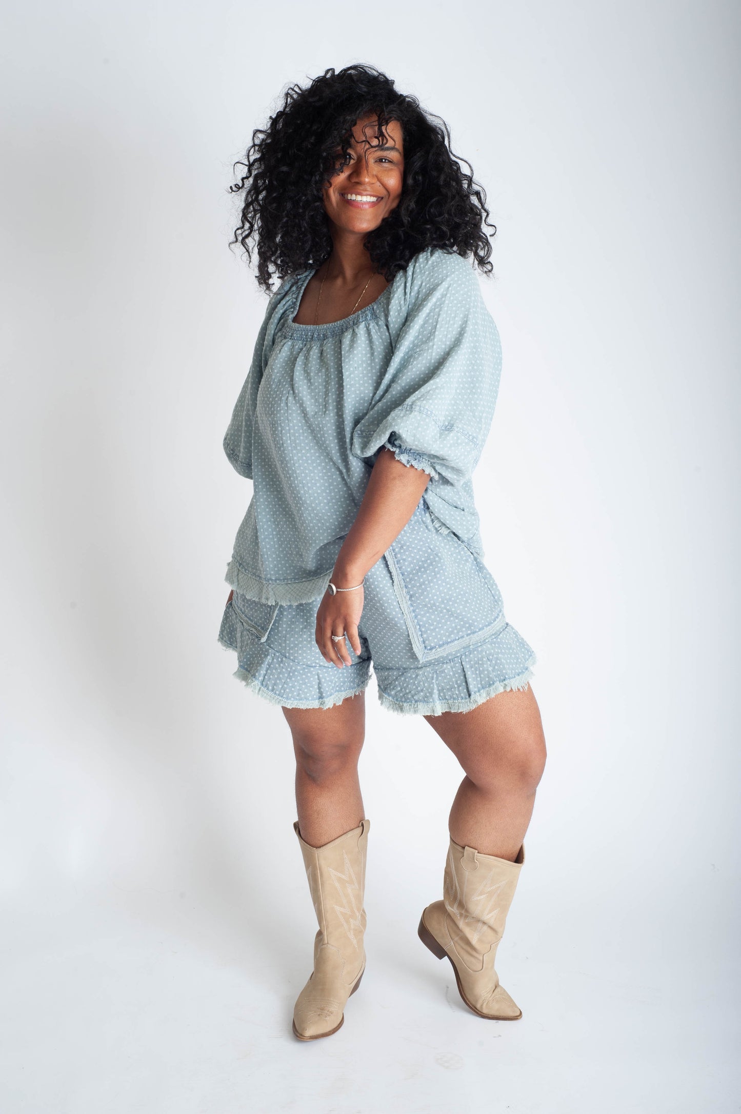 Woman wearing a light blue outfit with ruffled shorts and beige boots on a white background