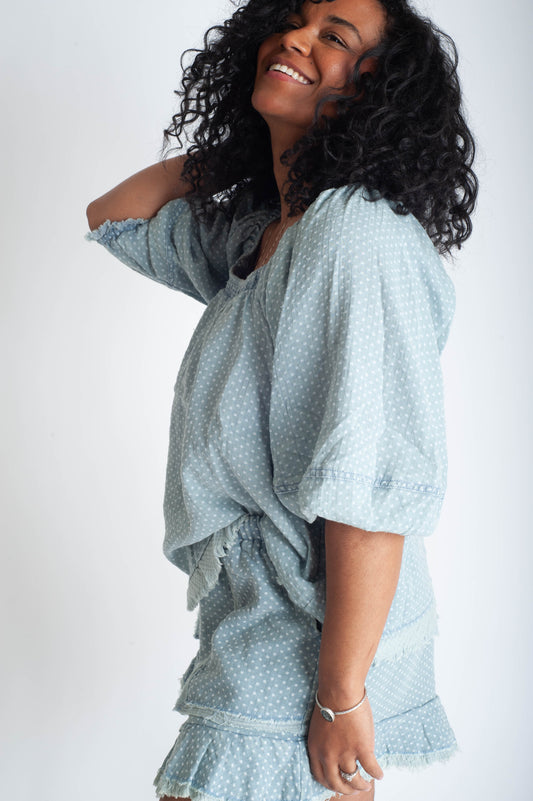 Woman wearing a light blue dress with ruffled sleeves and hem on a white background