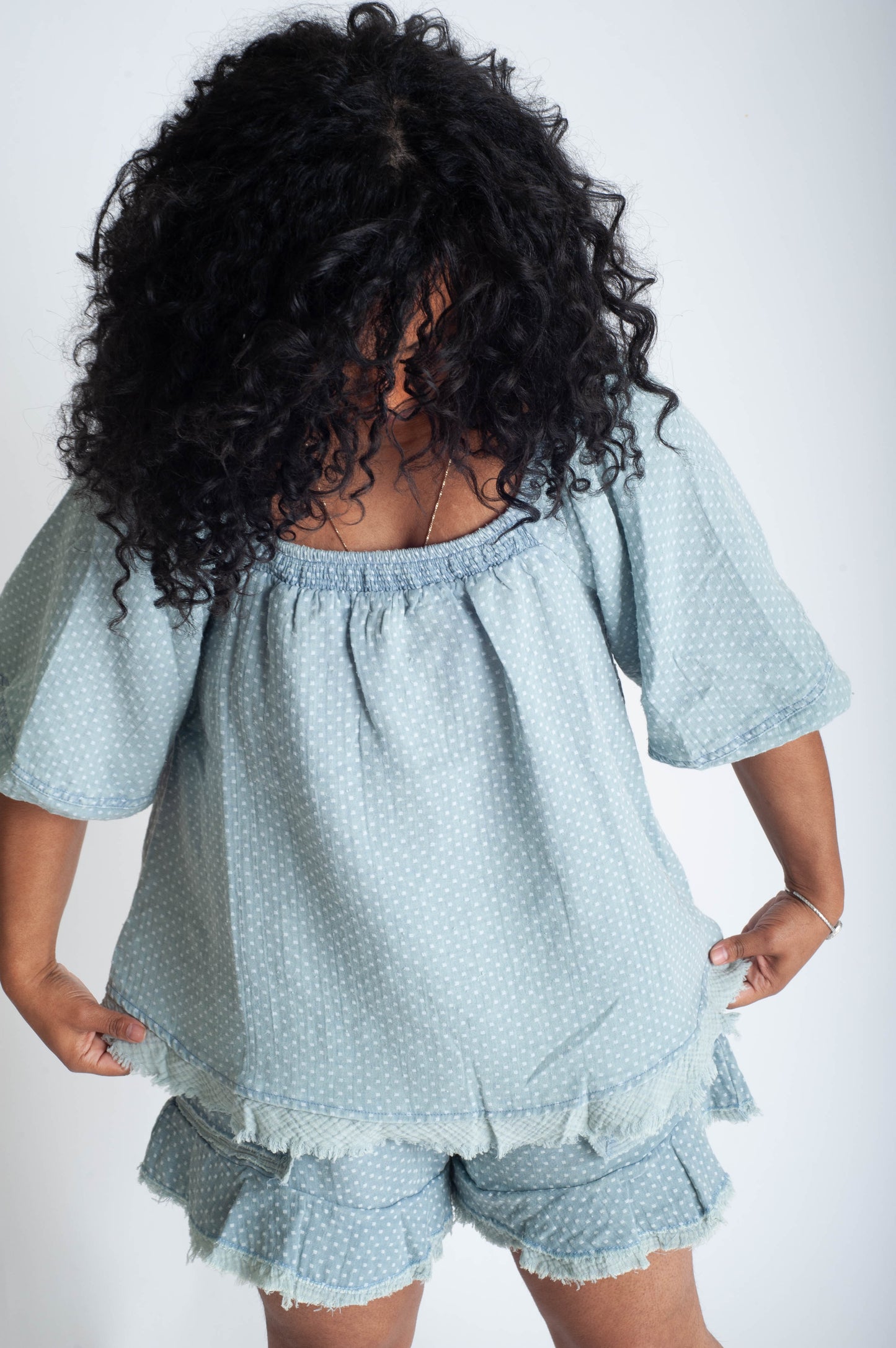 Person wearing a light blue textured top and shorts set on a white background