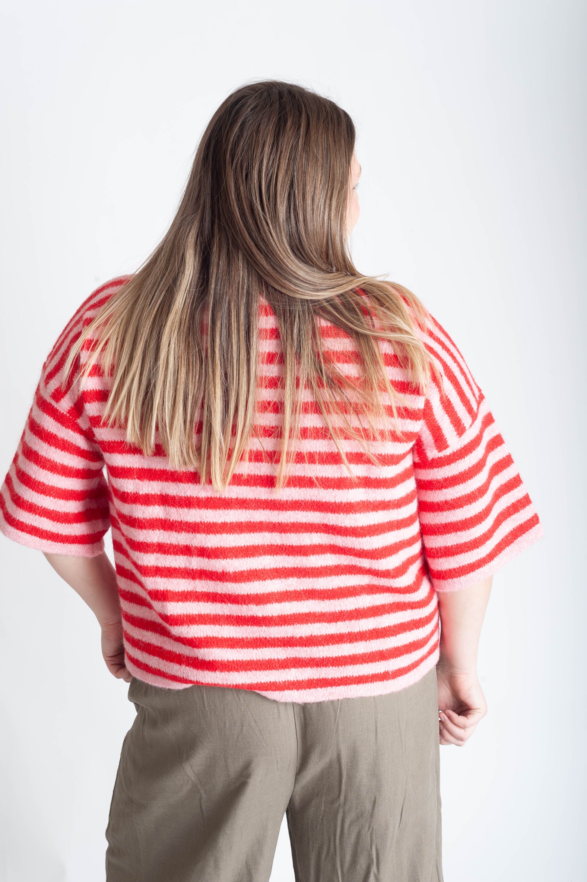 Women wearing a pink and red striped cardigan on a white background. 