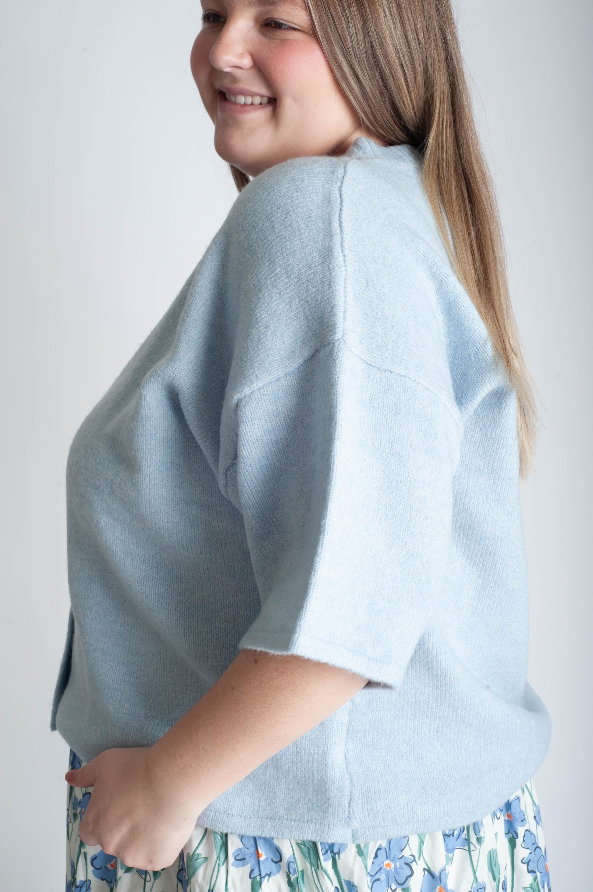 Person wearing a light blue cardigan over a floral dress on a plain background