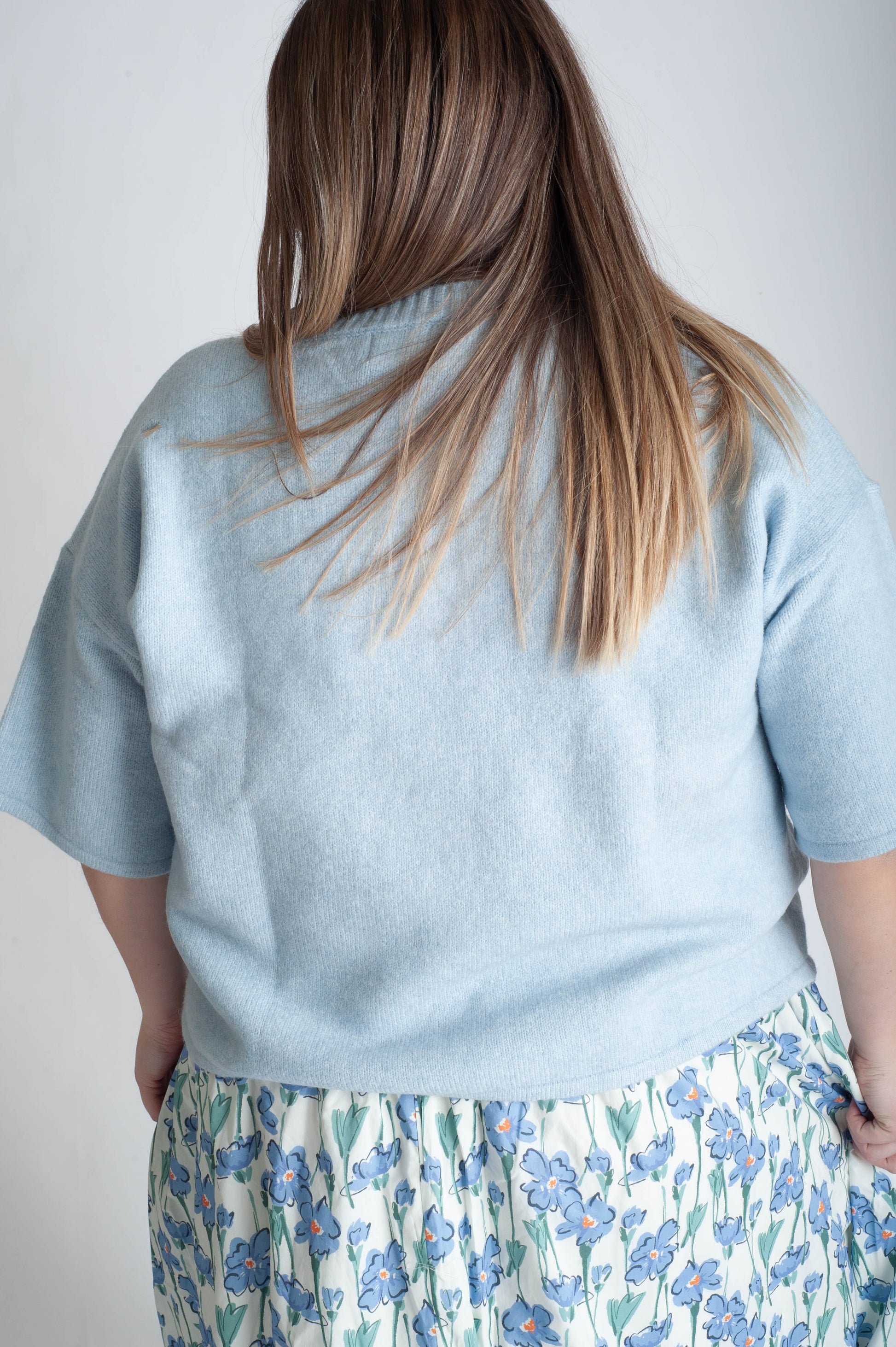 Person wearing a light blue shirt and floral skirt on a plain background