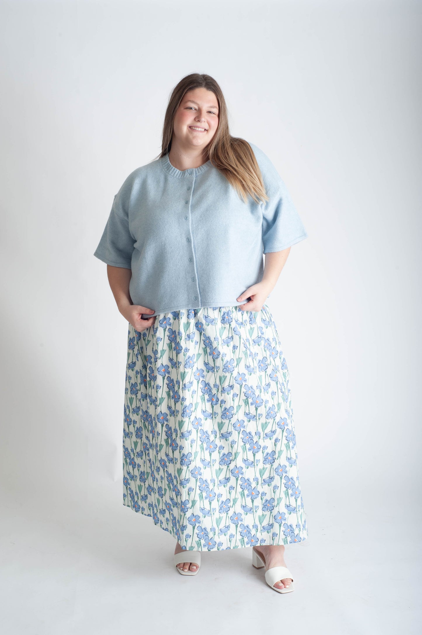 Woman wearing a light blue top and floral skirt on a white background