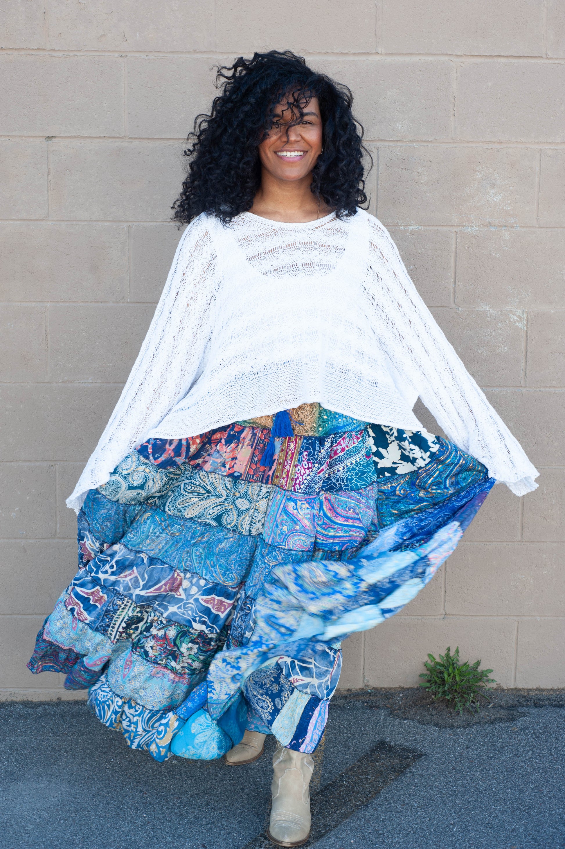 Woman wearing a white top and colorful patchwork skirt against a beige wall.