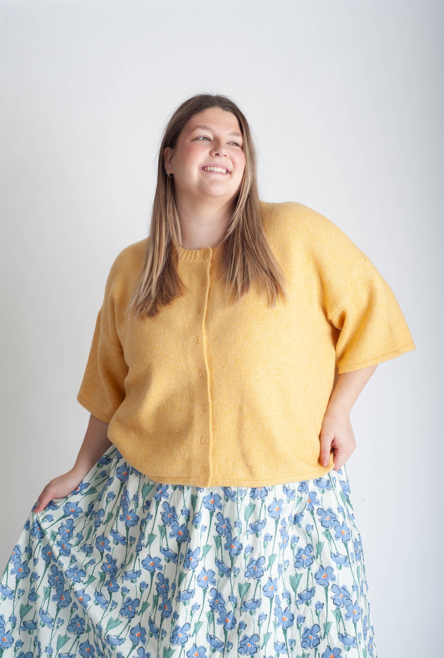Women wearing a yellow button up cardigan and blue floral skirt on a white background.