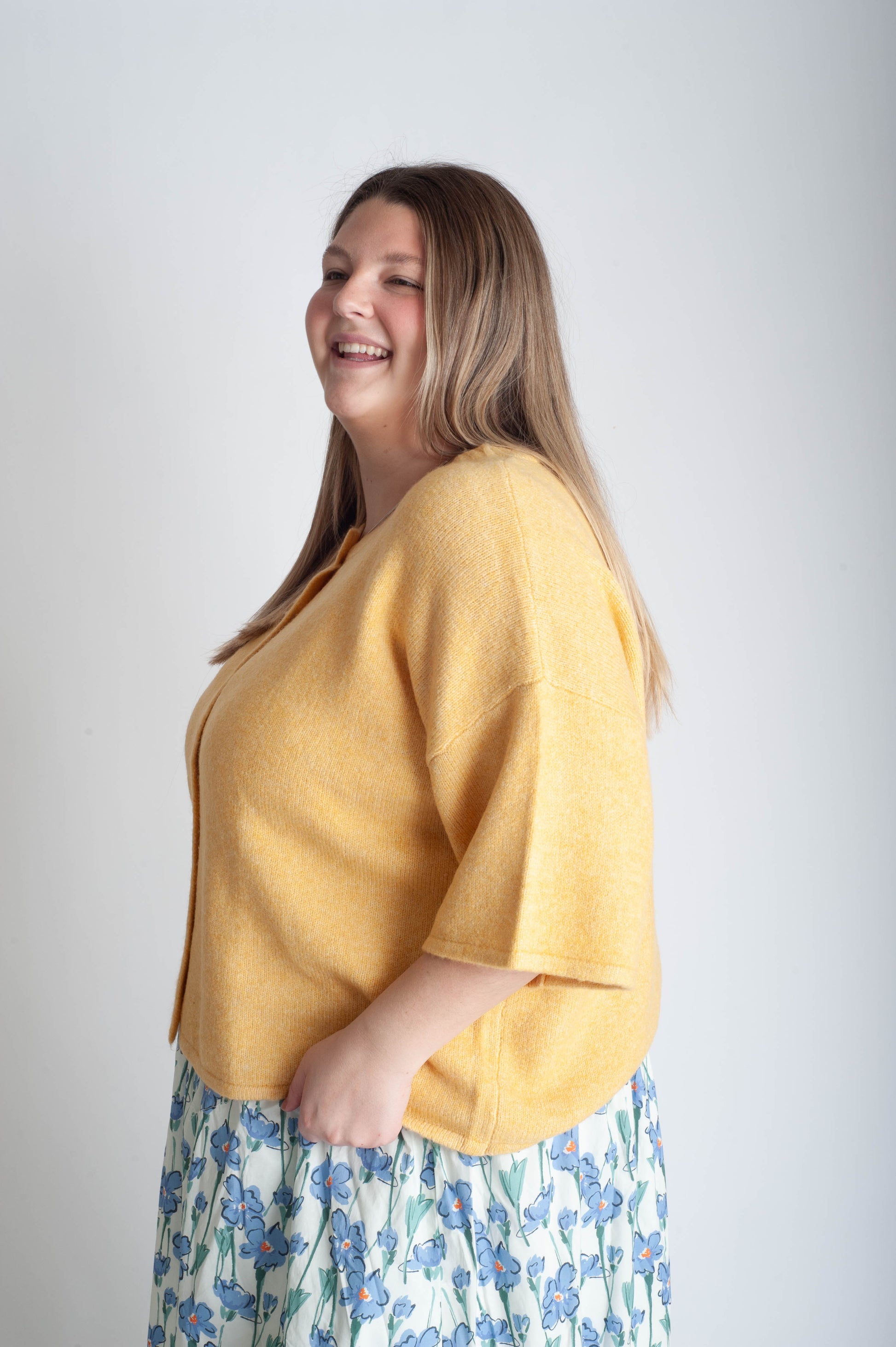 Woman wearing a yellow top and floral skirt against a plain background