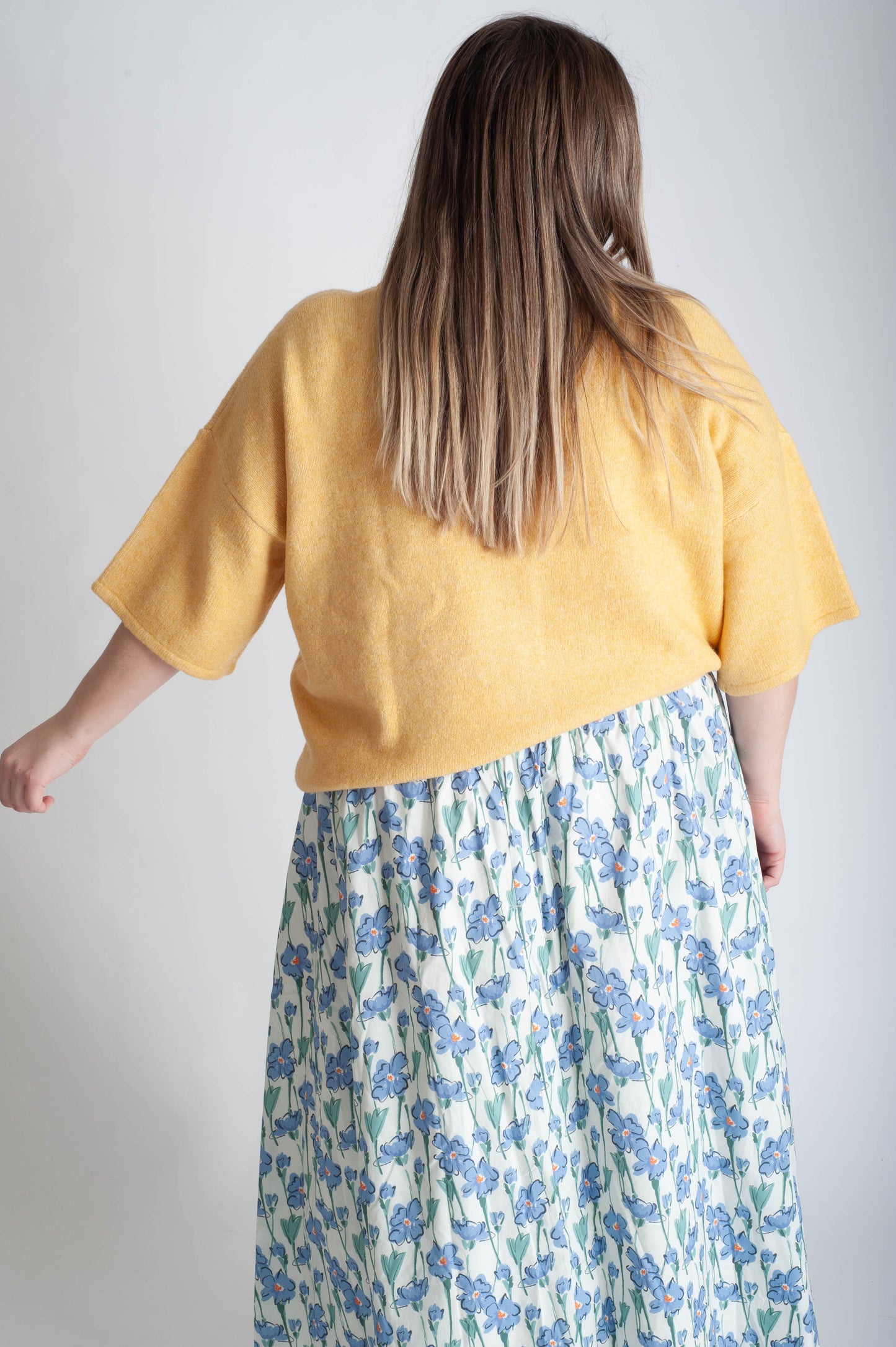 Women wearing a yellow button up cardigan and blue floral skirt on a white background.