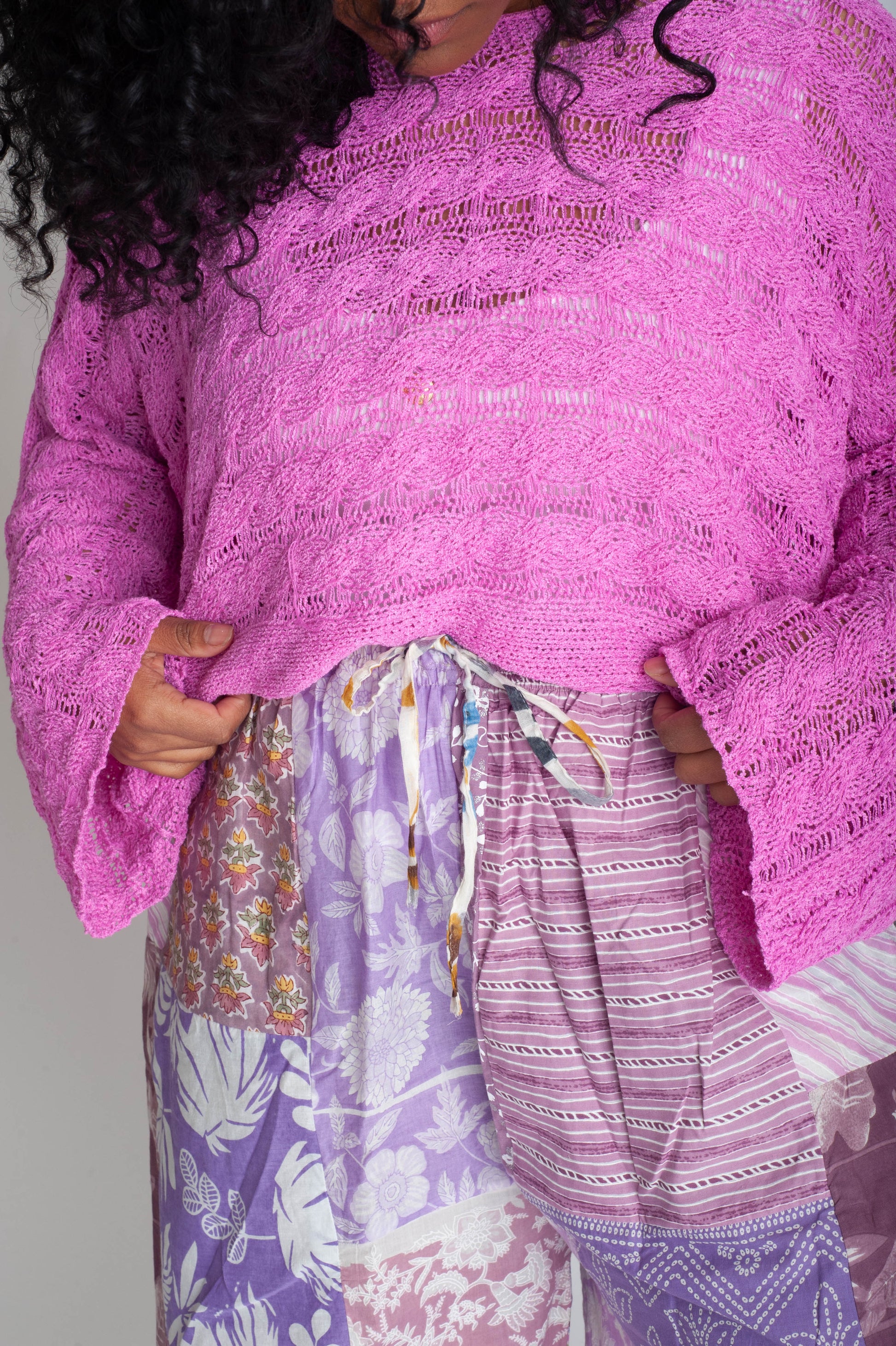 Person wearing a pink textured top and patterned pants against a neutral background
