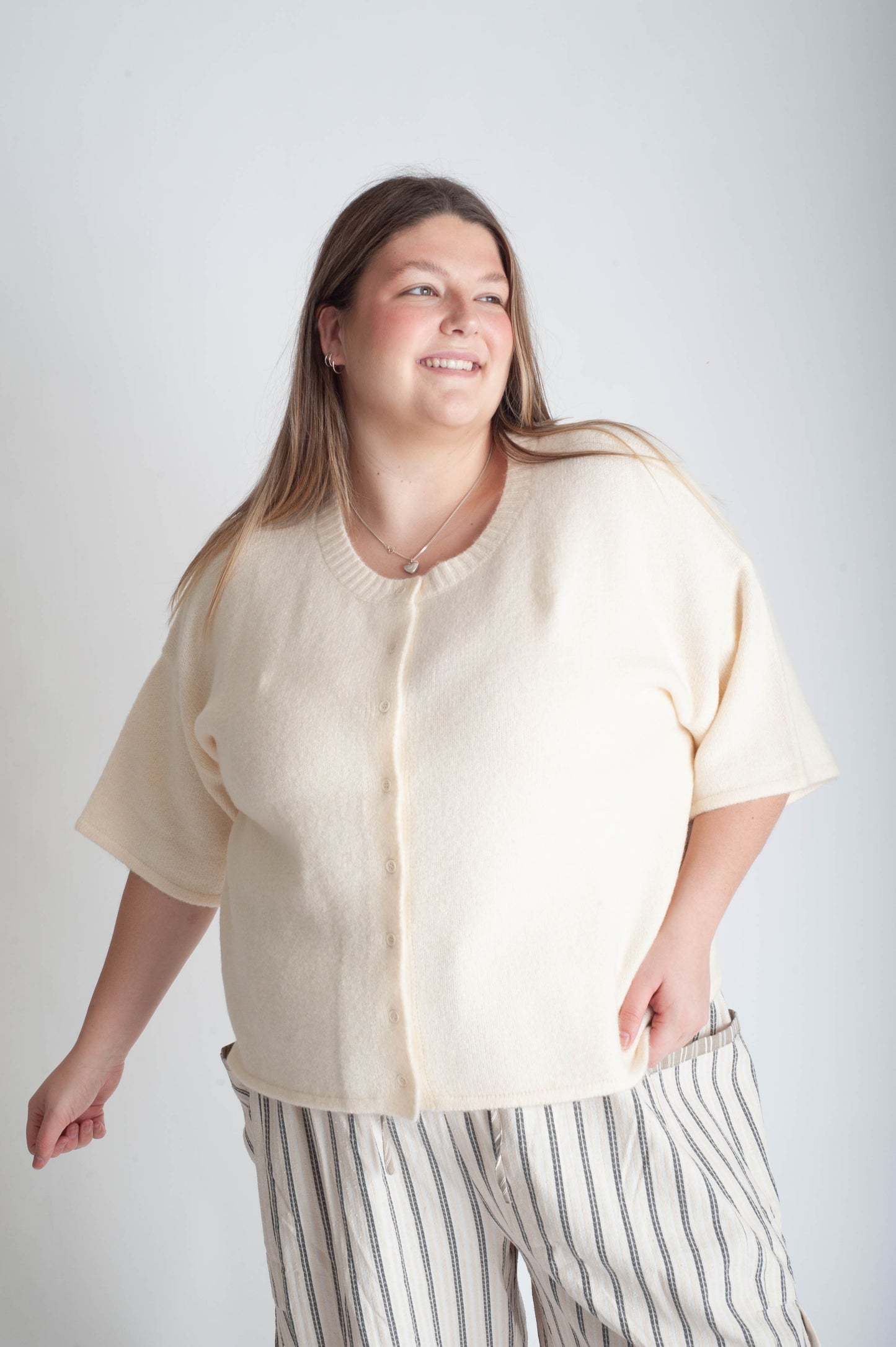 Woman wearing a beige cardigan and striped pants against a white background