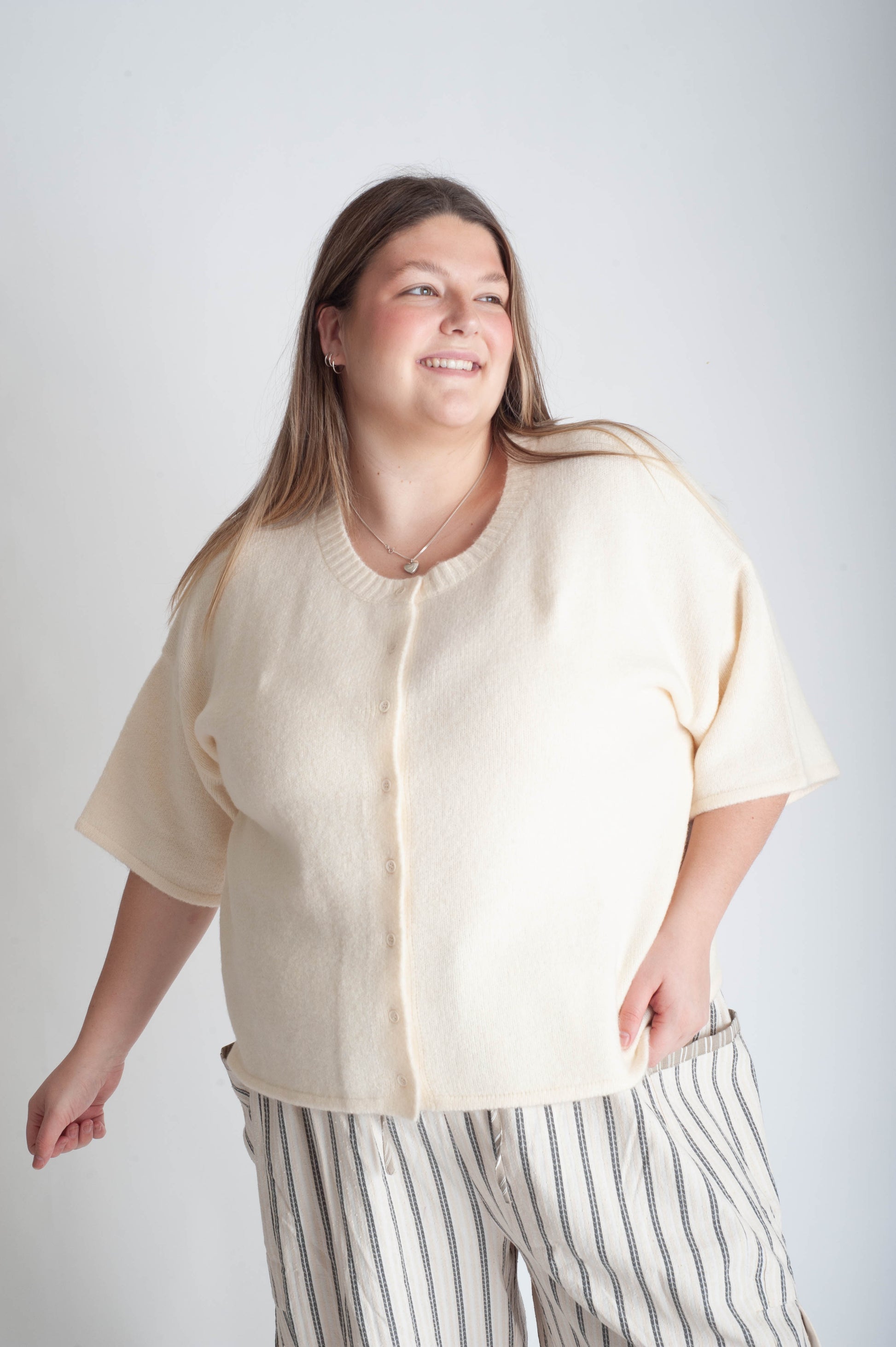 Woman wearing a beige cardigan and striped pants against a white background