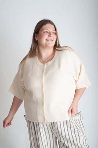 Woman wearing a beige cardigan and striped pants against a white background