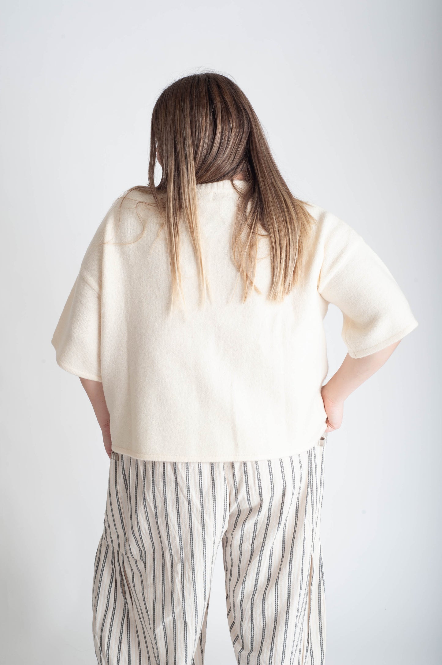 Person wearing a light-colored shirt and striped pants on a white background