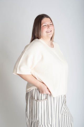 Women wearing a beige button up cardigan and blue floral skirt on a white background.