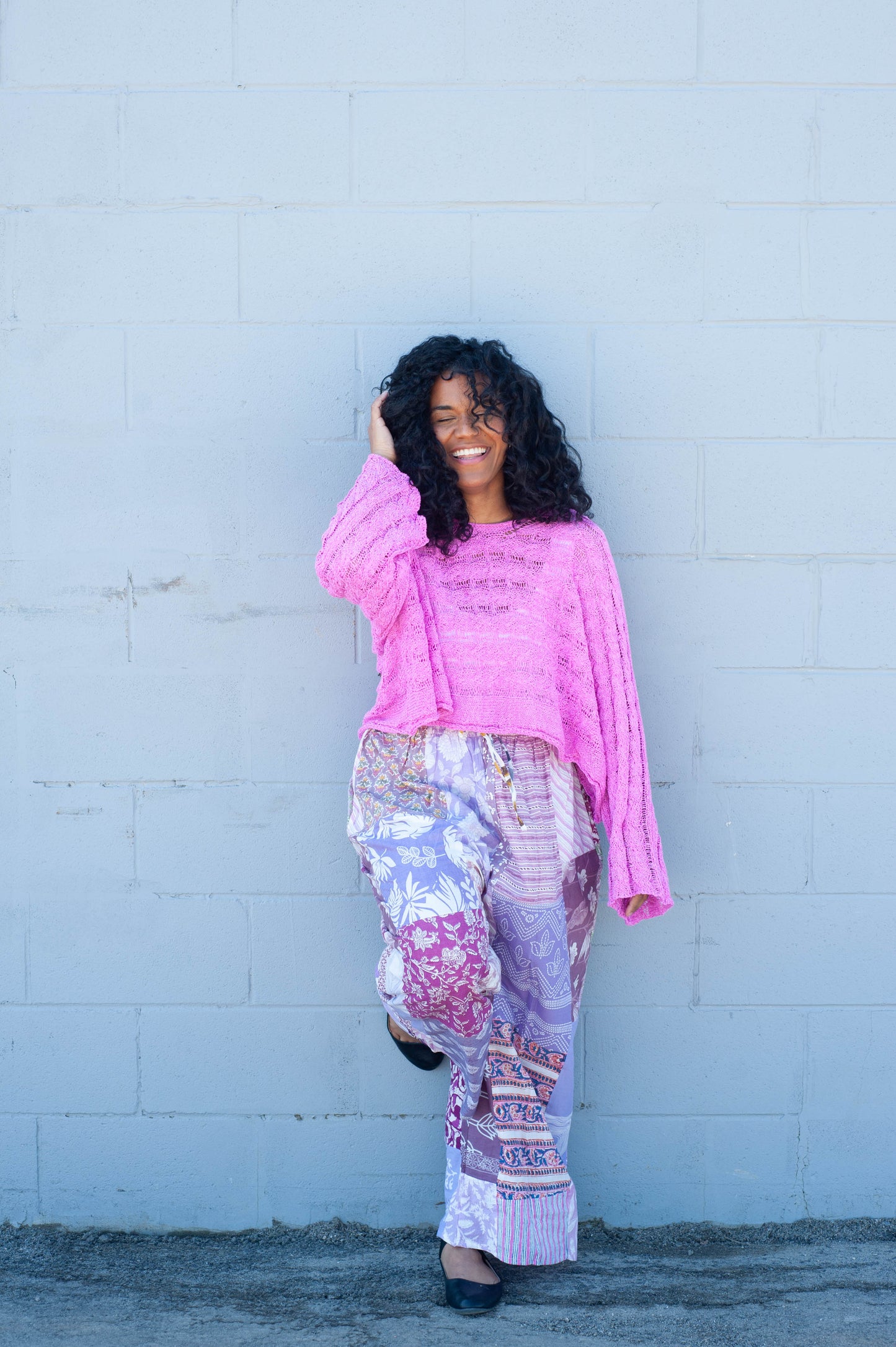 Woman wearing a pink top and patterned pants against a light blue wall.