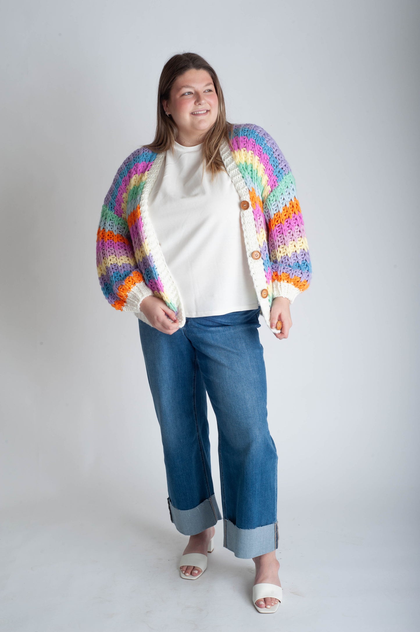 Person wearing a colorful cardigan over a white shirt and blue jeans on a plain background