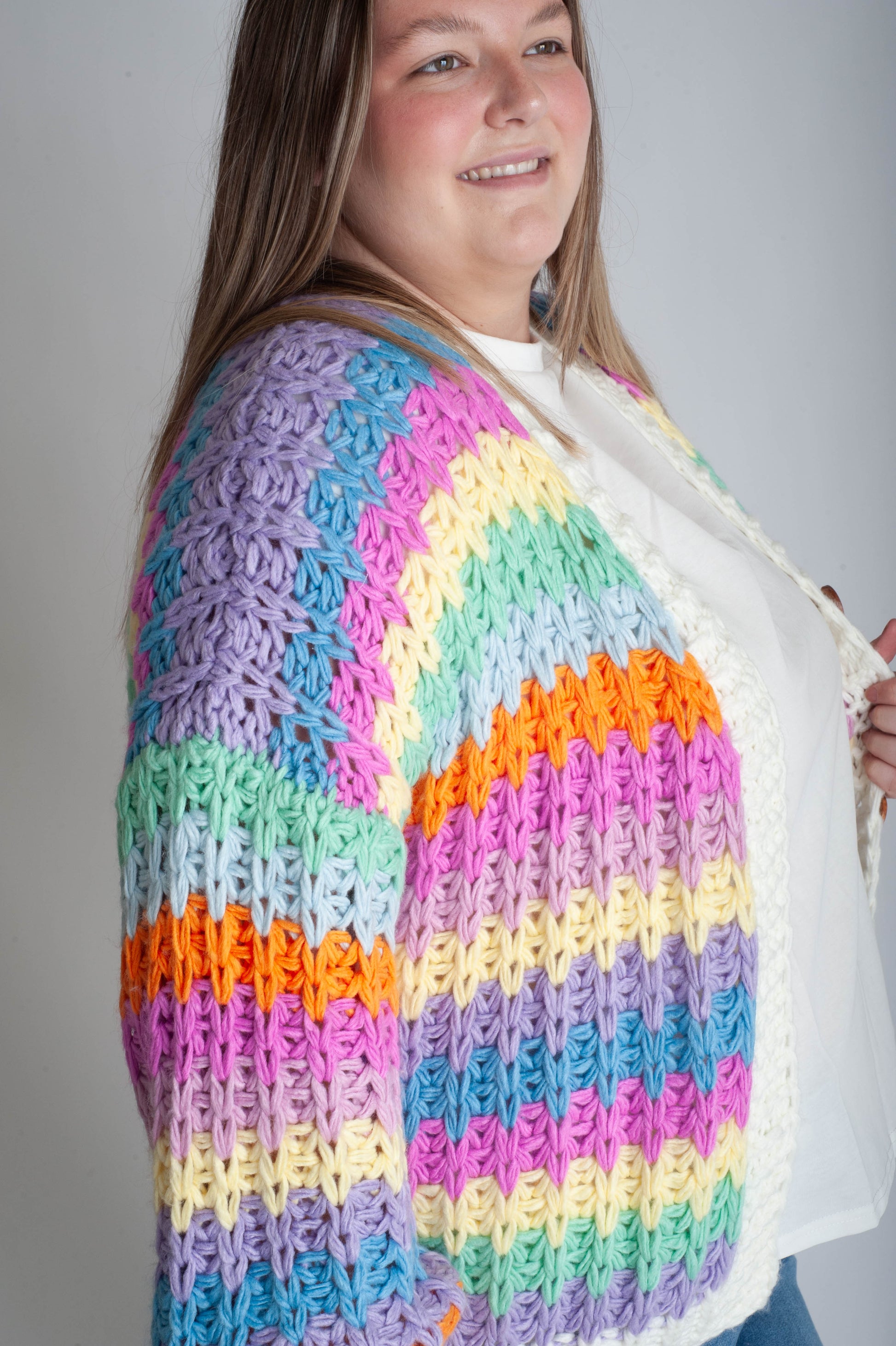 Woman wearing a colorful crocheted cardigan against a plain background