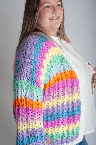 Woman wearing a colorful crocheted cardigan against a plain background