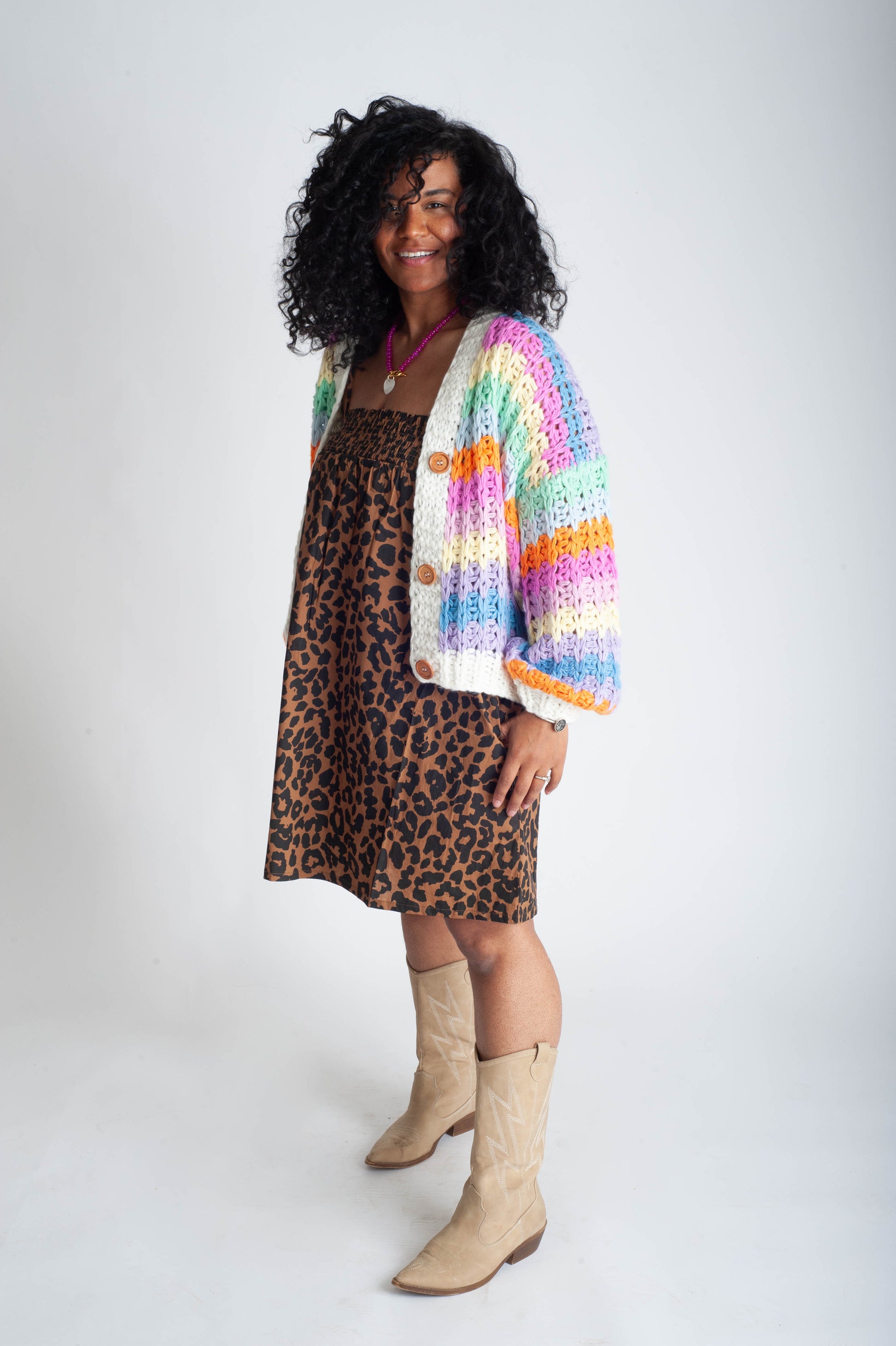 Woman wearing a colorful cardigan over a leopard print dress with beige boots on a white background