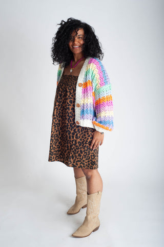 Woman wearing a colorful cardigan over a leopard print dress with beige boots on a white background