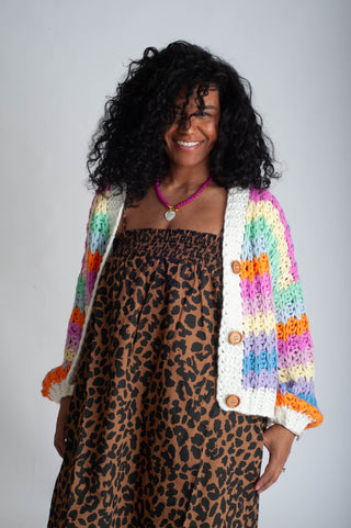 Woman wearing a colorful crochet cardigan over a leopard print dress on a plain background