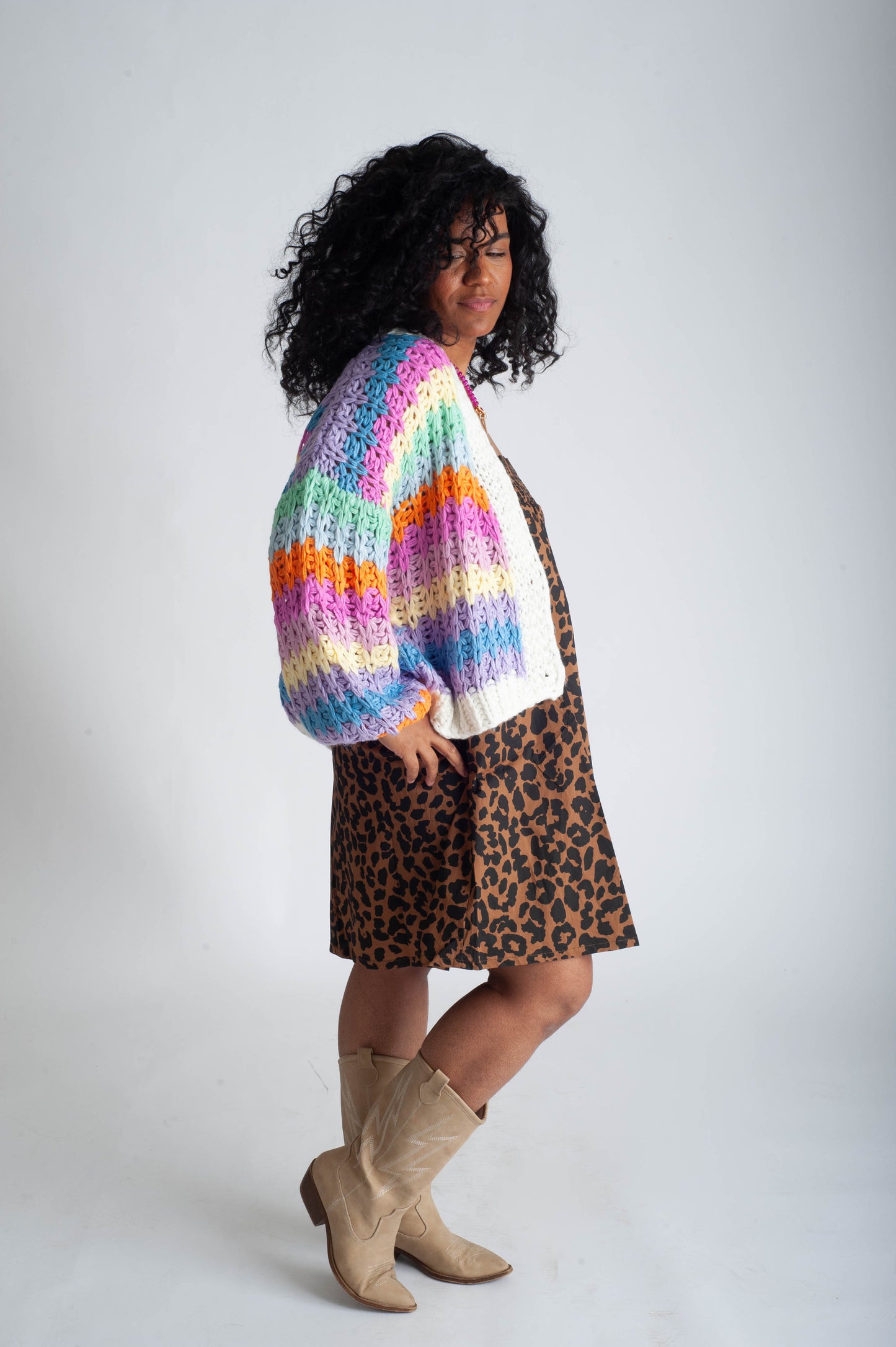 Person wearing a colorful striped sweater, white shirt, leopard print skirt, and beige boots on a plain background