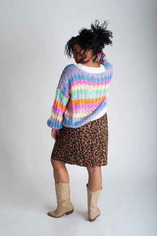 Person wearing a colorful striped sweater and leopard print skirt on a plain background